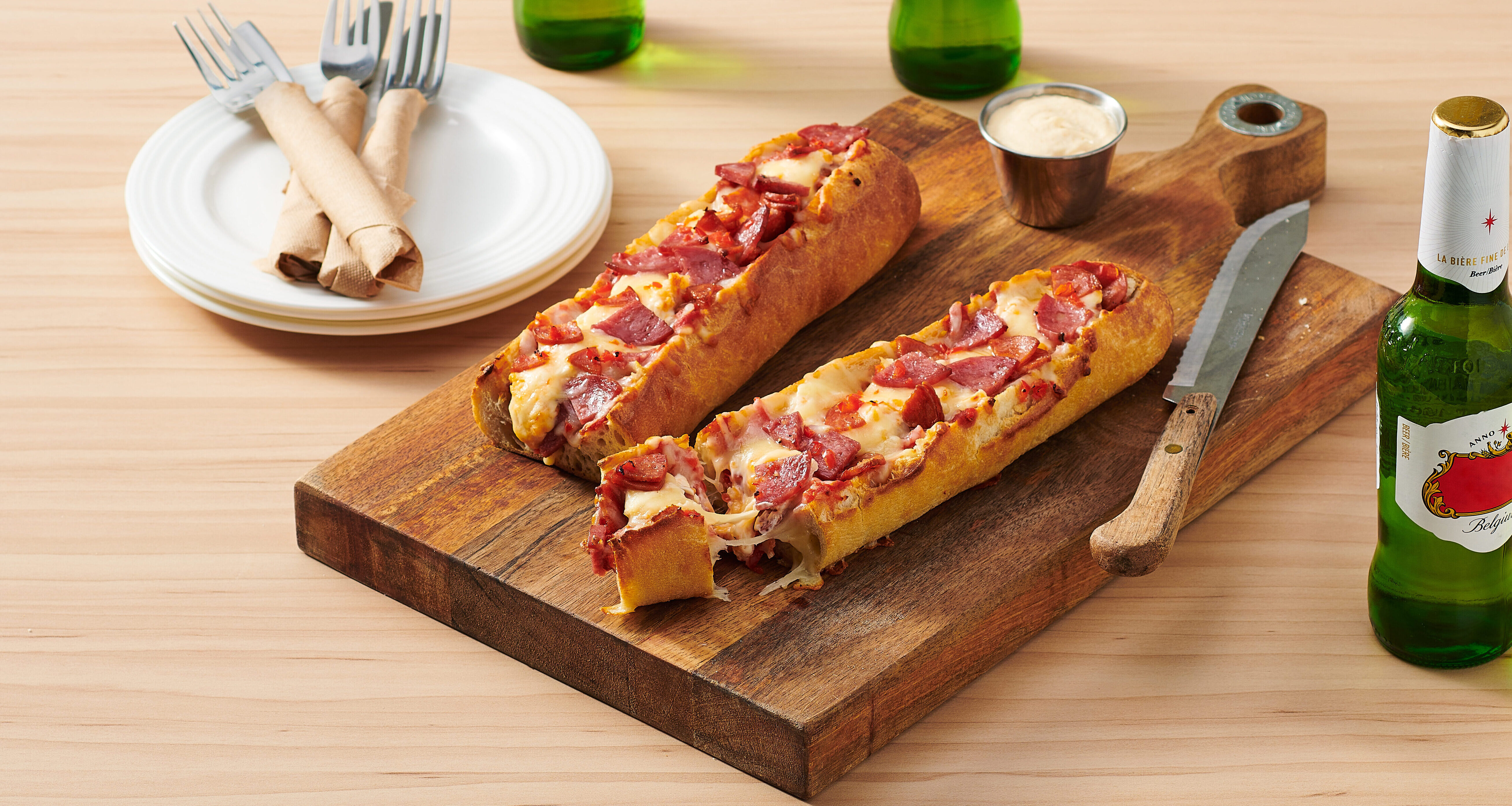 ACE Bakery® Foodservice White Baguette Pizza stuffed with cheese. Set in a restaurant menu inspired setting with a side butter and bottles of beer