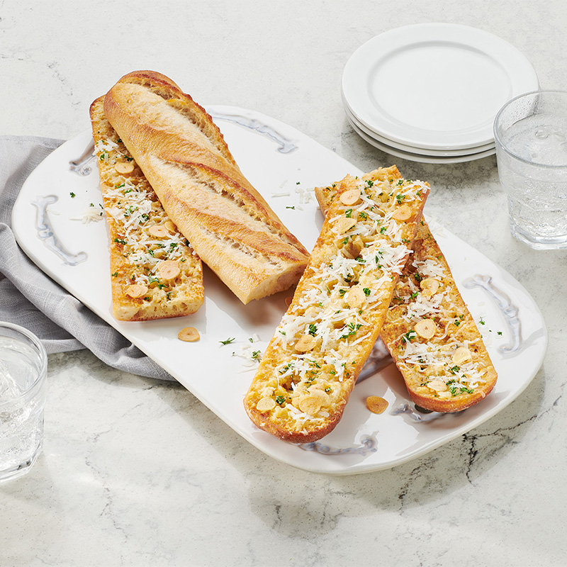 ACE Bakery® Foodservice White Baguette served as an elevated garlic bread with lots of parmesan cheese, plated as an elevated table bread service to share with the table.